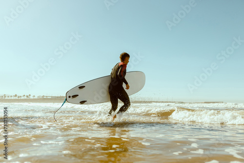 Side view of male surfer in wetsuit with his surfboard entering the sea. Surfing on ocean