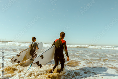 Back view of surfers with surfboards entering towards ocean for surfing on waves