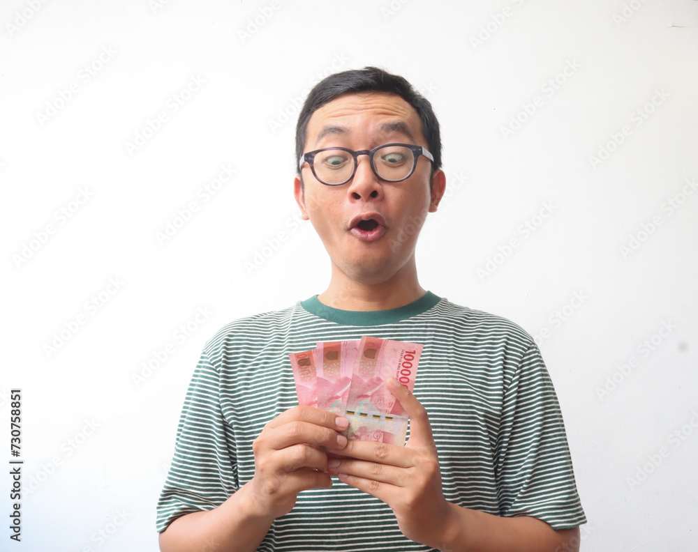 an asian adult man smiling while holding paper money or bank note with happy expression an asian adult man smiling while holding paper money or bank note with happy expression