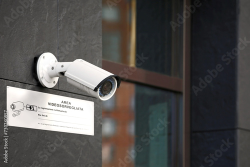 Primo piano di una telecamera di videosorveglianza sul muro di un edificio con cartello bianco 