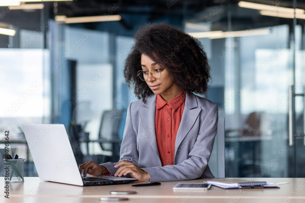Confident young businesswoman with curly hair working intently on her laptop in a stylish office environment. Confident young businesswoman with curly hair working intently on her laptop in a stylish office environment.