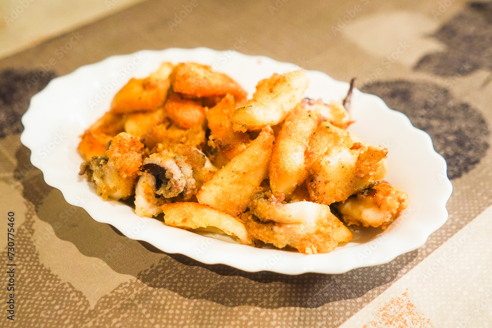 Fried cuttlefish on a white plate with a textured backdrop. Fried cuttlefish on a white plate with a textured backdrop.