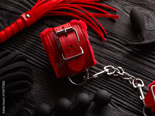 Red handcuffs and accessories for BDSM role play game over black wooden background