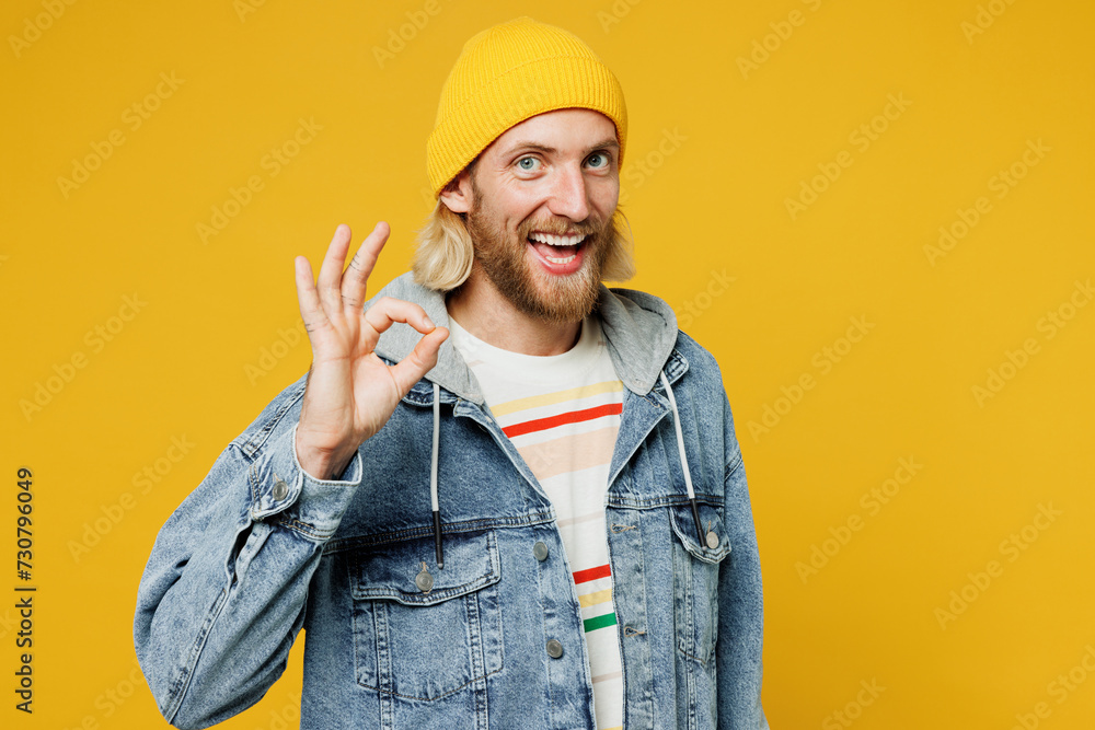 Young cheerful happy smiling satisfied fun blond man he wear denim shirt hoody beanie hat casual clothes showing okay ok gesture isolated on plain yellow background studio portrait. Lifestyle concept Young cheerful happy smiling satisfied fun blond man he wear denim shirt hoody beanie hat casual clothes showing okay ok gesture isolated on plain yellow background studio portrait. Lifestyle concept