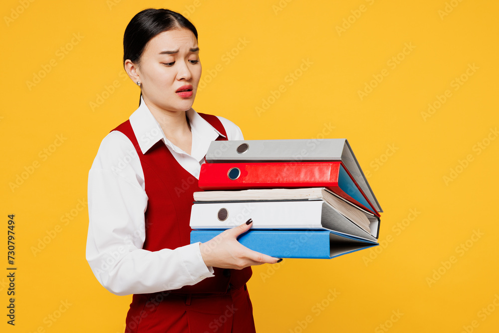 Young shocked lawyer employee business woman of Asian ethnicity wear red vest shirt work at office hold pile of folders papers document bookkeeping isolated on plain yellow background. Career concept. Young shocked lawyer employee business woman of Asian ethnicity wear red vest shirt work at office hold pile of folders papers document bookkeeping isolated on plain yellow background. Career concept.