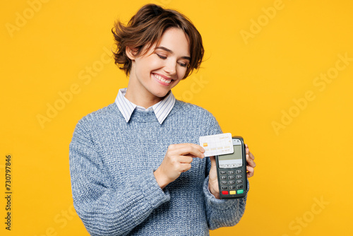 Young woman she wears grey knitted sweater shirt casual clothes hold wireless modern bank payment terminal to process acquire credit card isolated on plain yellow background studio. Lifestyle concept.