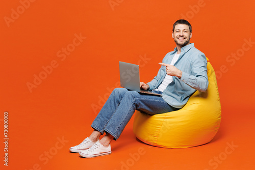 Full body young IT man wears blue shirt white t-shirt casual clothes hold use work point index finger on laptop pc computer isolated on plain red orange background studio portrait. Lifestyle concept.