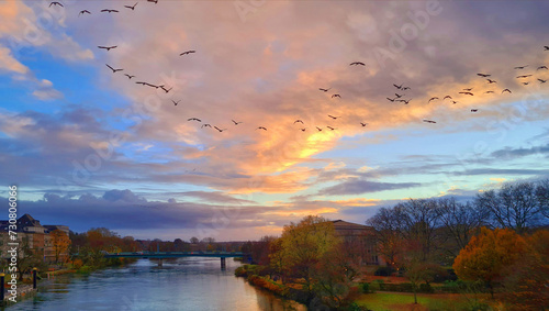 Foto migratory birds flying in v-shape below v-shaped cloudscape above a river at sun