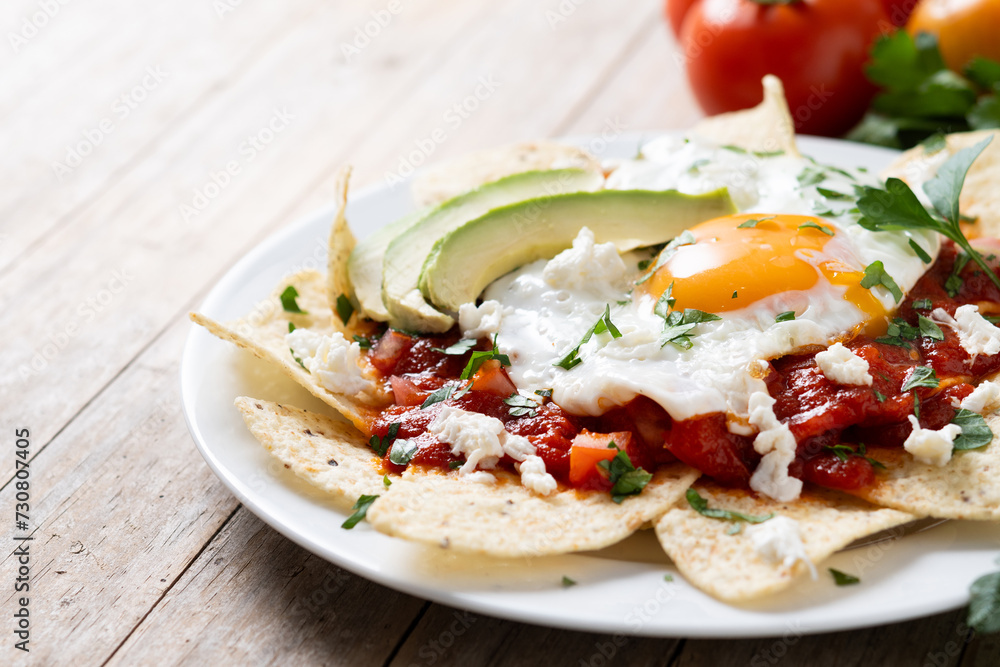 Traditional Mexican breakfast red chilaquiles with egg on wooden table. 