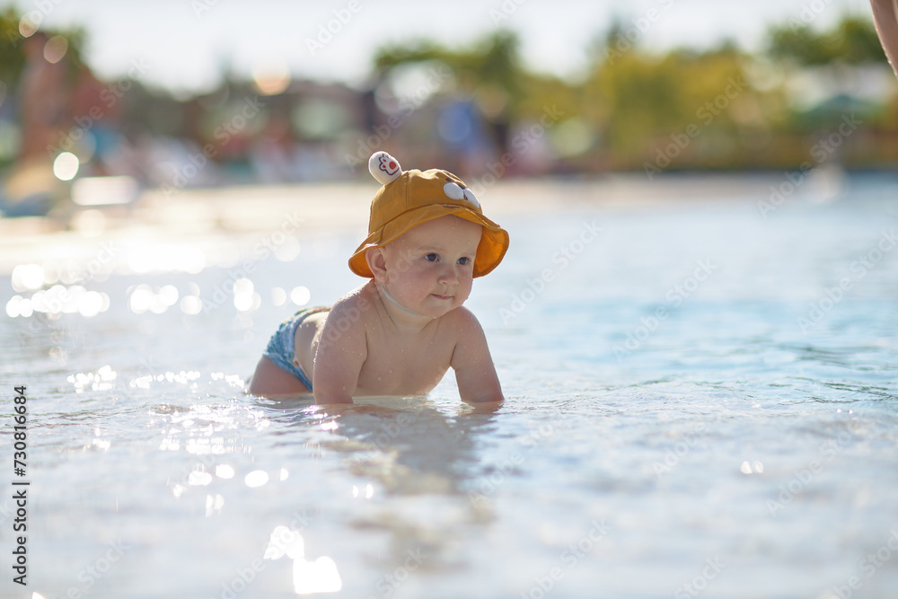 a little half a year old, a baby baby crawling on the water, smiling, outdoors, in a panama hat, in diapers, in the sun at the resort. a little half a year old, a baby baby crawling on the water, smiling, outdoors, in a panama hat, in diapers, in the sun at the resort.
