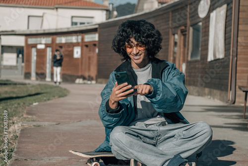 young teenager sitting on skateboard using mobile phone