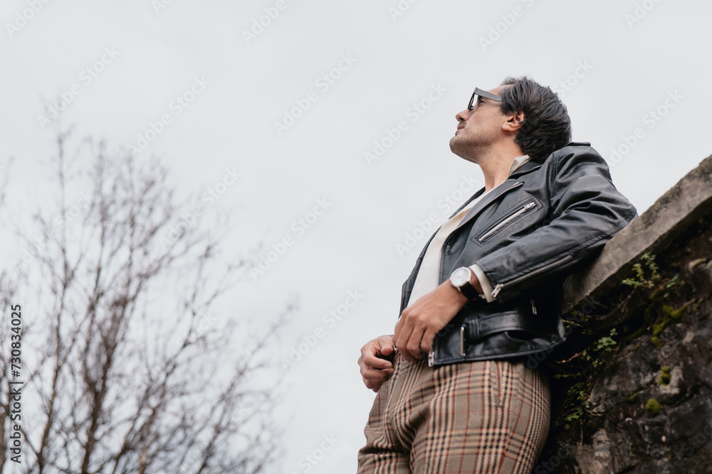 Adult Caucasian man wearing sunglasses and a black leather jacket outdoors. Adult Caucasian man wearing sunglasses and a black leather jacket outdoors.
