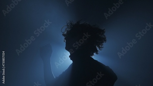 Male model against bright light on black background in studio. Man clubber silhouette dancing surrounded by rays of light in darkness.