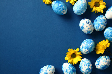 Blue and white painted Easter eggs on dark blue background with yellow flowers. Flat lay, top view, copy space