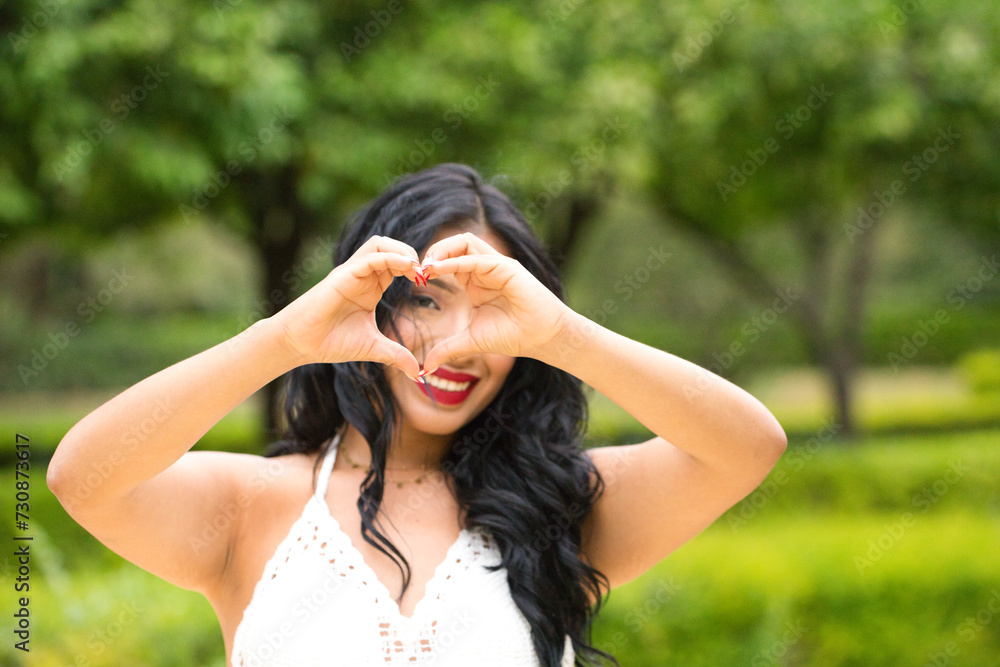 Young and beautiful brunette woman and latin, making a heart shape with her hand and fingers smiling looking through the sign. Concept friendship and love. 14 of february valentine's day.