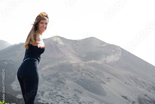 standing woman smiles extends her hand looking at camera in a volcano