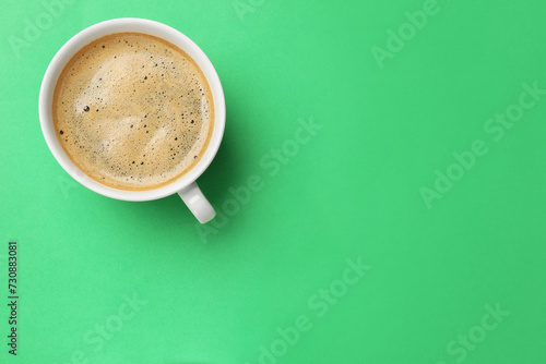 Aromatic coffee in cup on green background, top view. Space for text