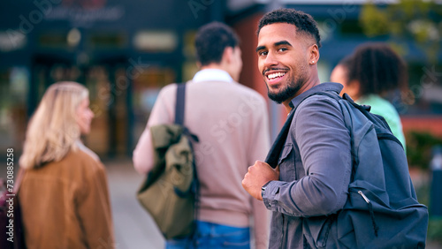 Portrait Of Male University Student Looking Over Shoulder With Friends Outside College Buildings