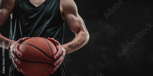 A focused athlete in a dark jersey holds a basketball against a dark background, emphasizing the readiness and determination for the game. 