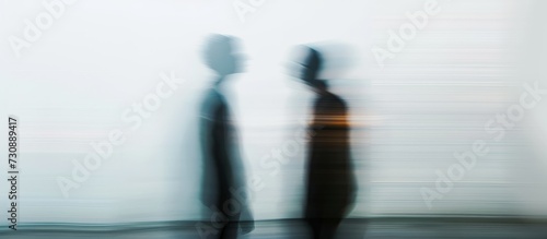A monochrome photograph of two people standing side by side, their shadows creating blurred and dark figures against a room's horizon. The electric blue tint adds a hint of color.