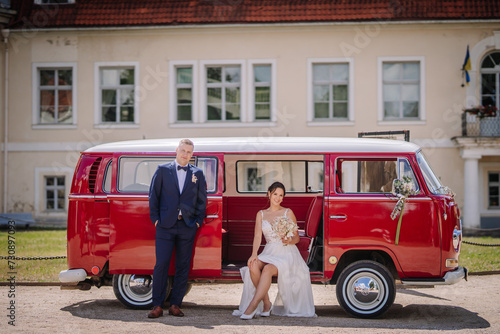 Valmiera, Latvia - July 7, 2023 - ide and groom with a red vintage van, building in the background