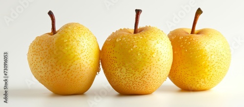 Three yellow apples, a type of natural food and staple ingredient, are placed together on a white surface.