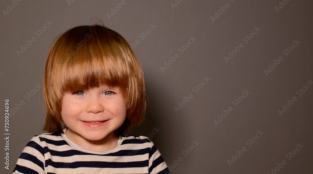 Child's face Portrait of a smiling little boy. Radiant smile, preschool boy with long blond hair. Space for text, gray background Child's face Portrait of a smiling little boy. Radiant smile, preschool boy with long blond hair. Space for text, gray background