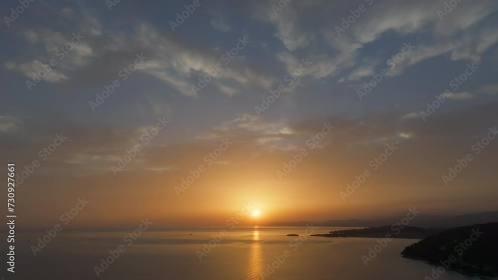 Aerial shot of a drone flying forward towards a stunning sunset, with clouds scattered across the golden-hued sky above the calm sea Aerial shot of a drone flying forward towards a stunning sunset, with clouds scattered across the golden-hued sky above the calm sea