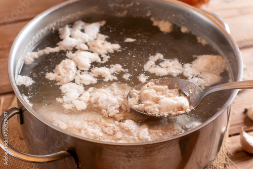 Cooking meat in a aluminum saucepan. Foam on the surface of the water. Bone broth