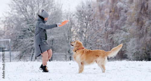 Girl Throwing Ring Toy To Adorable Golden Retriever Dog On A Snow Field In Winter