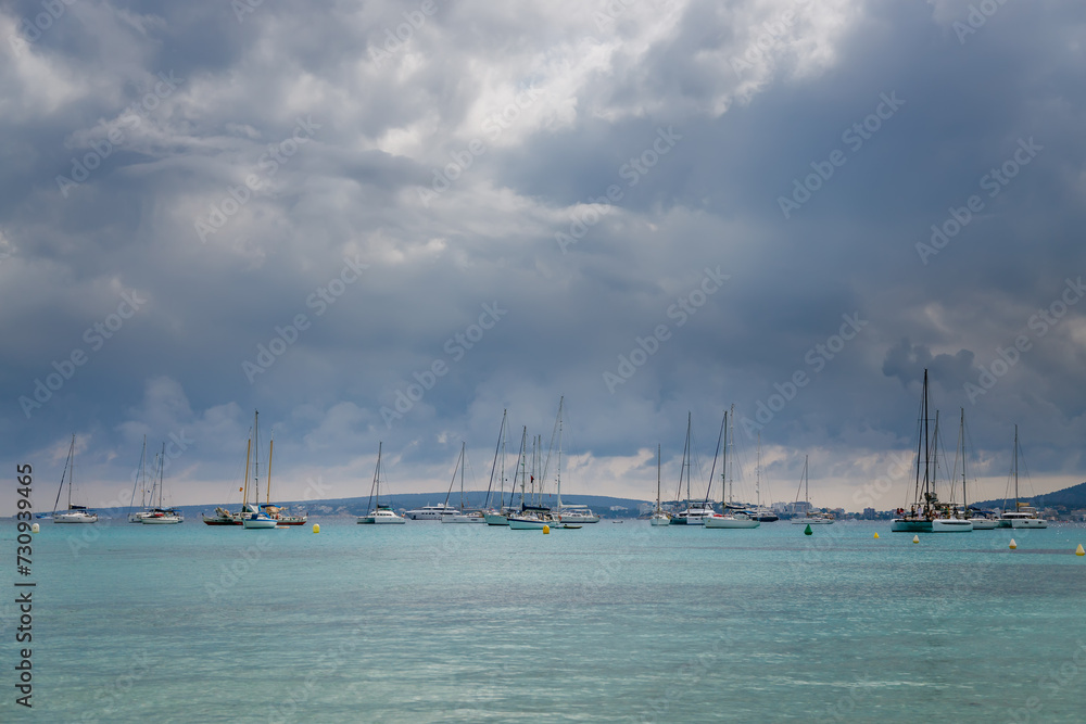 Fototapeta premium A serene seascape in Mallorca with multiple sailboats, peacefully anchored on calm turquoise waters