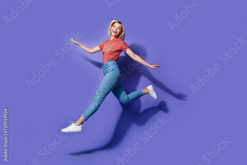 Full length size photo of overjoyed funny girl run air wear denim jeans with striped t shirt carefree isolated on purple color background