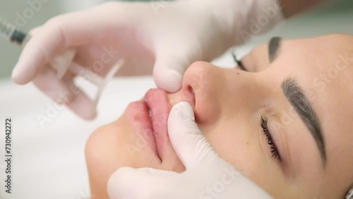 Beauty injections. Lip augmentation procedure. Lip injection. A cosmetologist in medical gloves gives a beauty injection to a young client in a medical cabin.