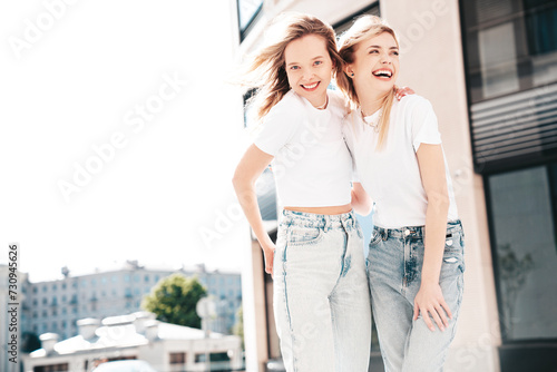 Two young beautiful smiling hipster female in trendy summer white t-shirt and jeans clothes. Carefree women posing in the street. Positive models having fun outdoors. Cheerful and happy © halayalex
