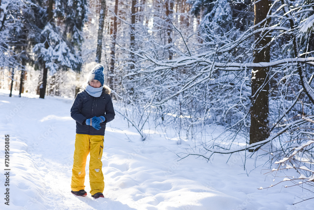 happy 11 year old boy walks in a snowy forest on a winter day in warm clothes. A joyful child walks in the forest on a sunny day