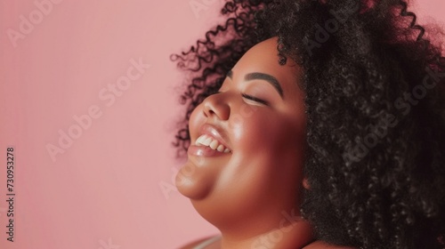 A joyful individual with a radiant smile closed eyes and curly hair against a soft pink background exuding a sense of happiness and contentment.