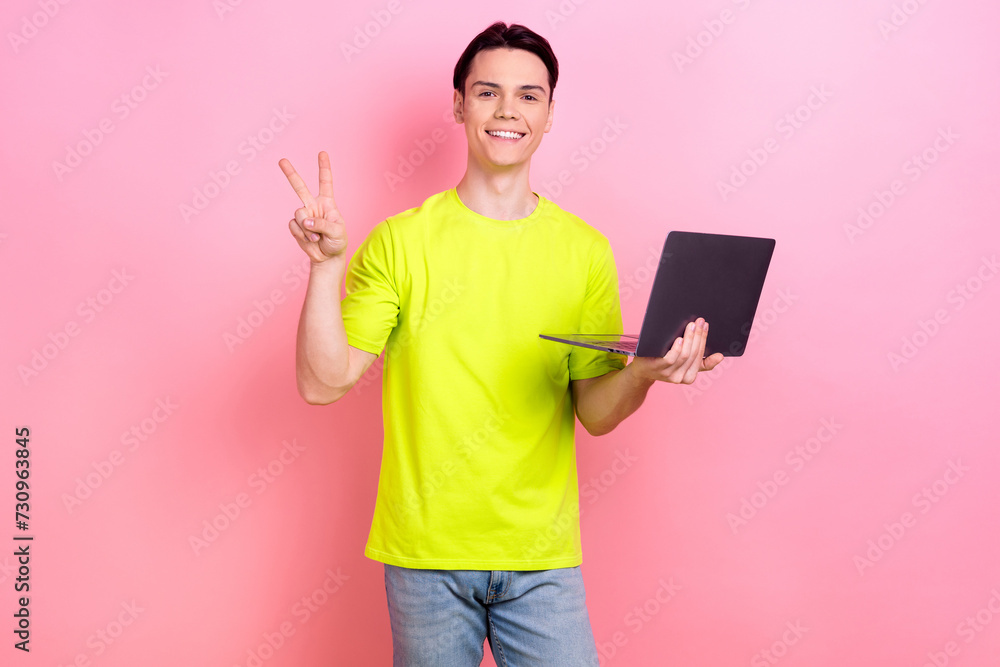 Photo portrait of handsome teen male show v-sign hold netbook wear trendy yellow garment isolated on pink color background
