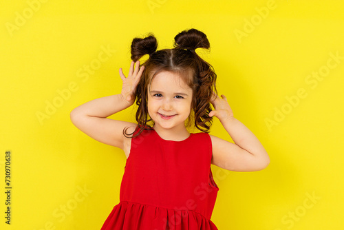 Cute little surprised happy girl in a red dress stands on a yellow background. card, banner. lifestyle. space for text. High quality photo