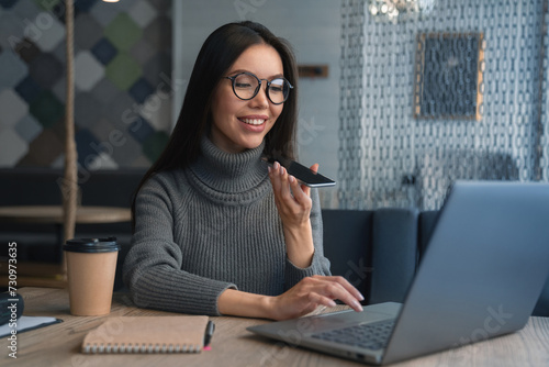 Bild auf Leinwand Happy business woman talking on speakerphone sitting at table with laptop, paper cup for coffee and notebook on it