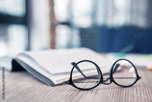 Eyeglasses at the wooden table with notebook on the background. Focus on glasses. Literature, studying, learning process, library concept. Knowledge and wisdom