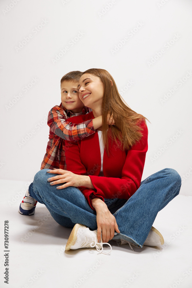 Family portrait of beautiful young mother embracing with little boy, son against white studio background. Casual style outfits. Concept of happiness, Mother's day, childhood, fashion and lifestyle Family portrait of beautiful young mother embracing with little boy, son against white studio background. Casual style outfits. Concept of happiness, Mother's day, childhood, fashion and lifestyle