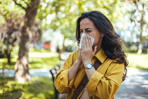 Portrait of unhealthy cute  female in yellow top with napkin blowing nose, looks to the source of the allergy, place for advertising. Rhinitis, cold, allergy concept. Pollen allergy symptoms photo