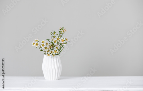 White small flowers in a vase on a table on a gray background in minimalist style, concept of minimalism, style, modern design