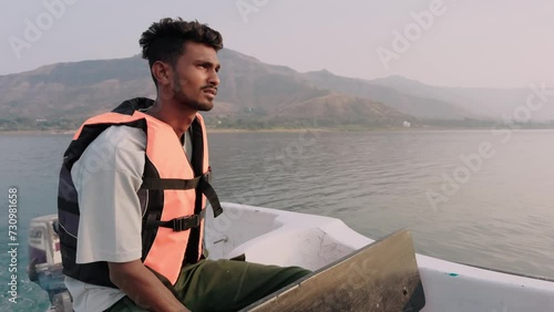 thoughtful Man in life jacket steering a boat with scenic mountain and lake in the background siting in a yacht and thinking
