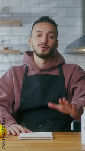 Vertical video. Vlogger man in an apron sit in kitchen talking to camera, recording video about making lemonade at domestic home. Online broadcast, man leads food blog or course