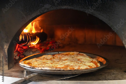 Baked tasty delicious pizza in a traditional oven with burning wood and shovel. 