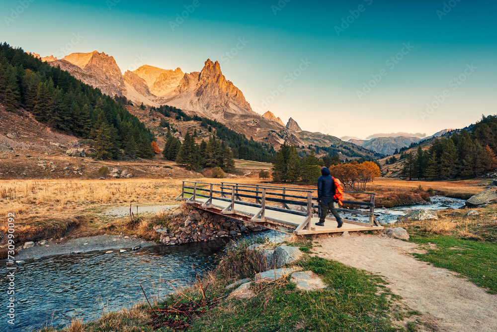 Sunrise over Claree valley and male tourist walking through wooden bridge in autumn at French Alps, France