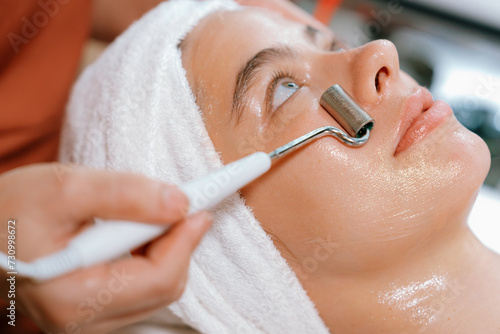 Beautiful caucasian woman lying on spa bed during having facial massage by professional hands at modern spa salon surrounded by beauty electrical equipment or medical equipment. Close up. Tranquility