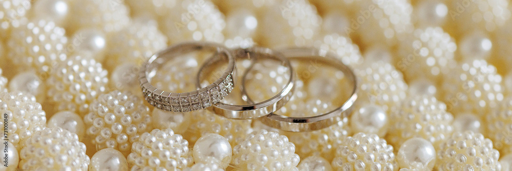 Three golden rings, one diamond-studded, rest on white pearls. Symbolizes a church engagement. The serene, elegant image evokes love and commitment. Banner with copy space. Three golden rings, one diamond-studded, rest on white pearls. Symbolizes a church engagement. The serene, elegant image evokes love and commitment. Banner with copy space.