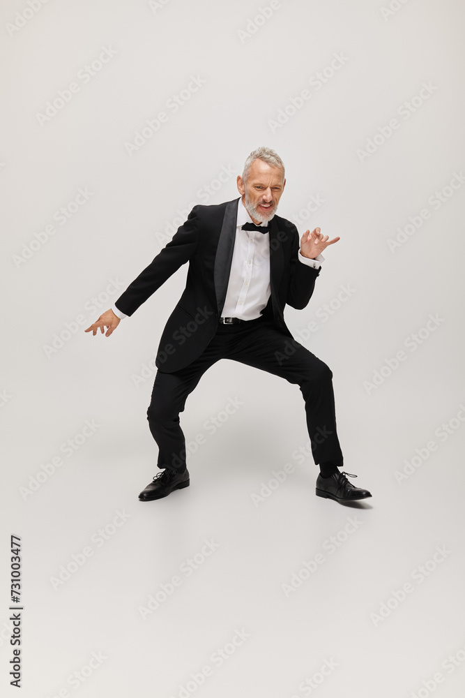 attractive jolly mature man with elegant dapper style with beard dancing happily on gray backdrop attractive jolly mature man with elegant dapper style with beard dancing happily on gray backdrop